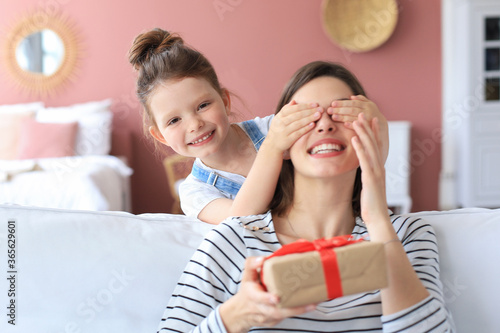 Little girl make birthday present to excited parent , smiling little child congratulate give gift box to happy mother and closed mother's eyes.