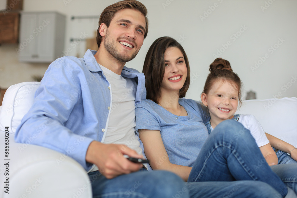 Happy family with child sitting on sofa watching tv, young parents embracing daughter relaxing on couch together. Happy family with child sitting on sofa watching tv, young parents embracing daughter relaxing on couch together.
