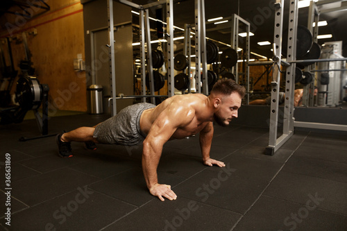 Sport motivation for people. Side view of young handsome man in sportswear doing push-up at gym