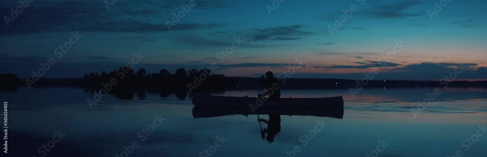 Man canoeing in a traditional wooden boat on a large lake at dawn. Shot on RED cinema camera with 2x anamorphic lens Man canoeing in a traditional wooden boat on a large lake at dawn. Shot on RED cinema camera with 2x anamorphic lens