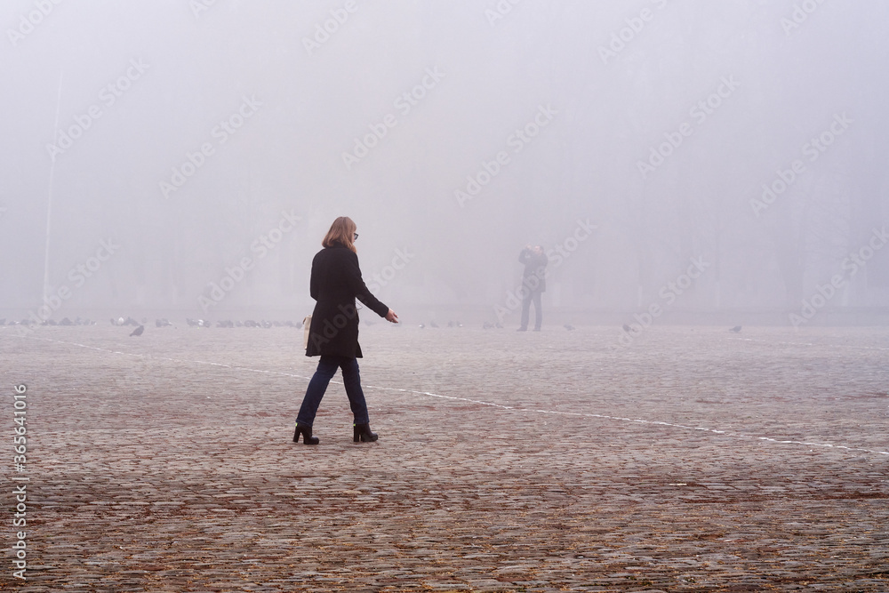 A woman walks through the city in foggy weather