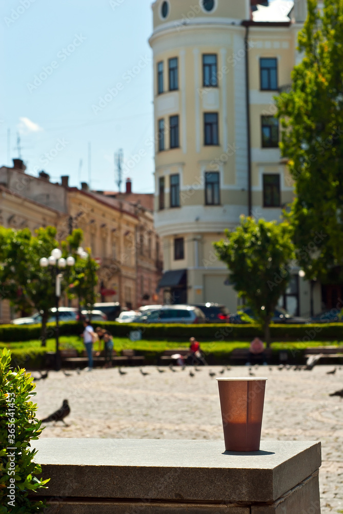Brown paper cup on a background of urban architecture. Coffee on a marble border. The houses of the old town are blurred in the background. Sharpness on coffee. Layout for design.