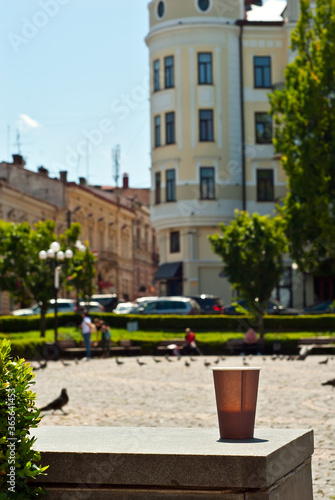 Brown paper cup on a background of urban architecture. Coffee on a marble border. The houses of the old town are blurred in the background. Sharpness on coffee. Layout for design.