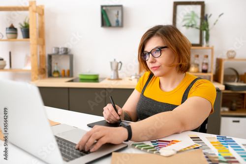 Young pretty confident designer looking at laptop display while drawing sketch