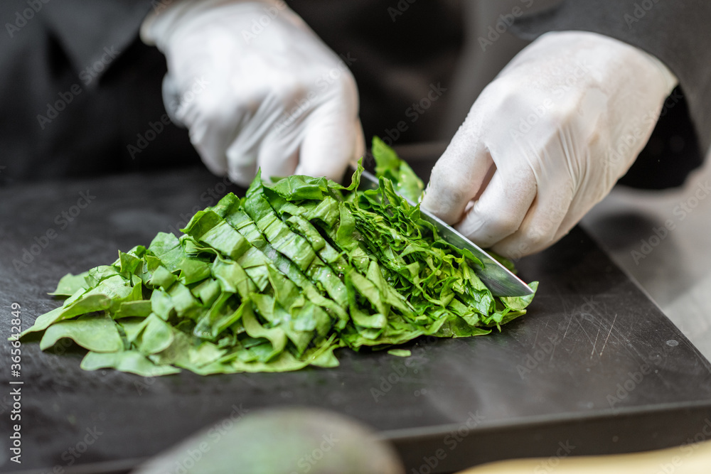 Chef in gloves cutting spinach on a cutting board at the kitchen, close-up Chef in gloves cutting spinach on a cutting board at the kitchen, close-up