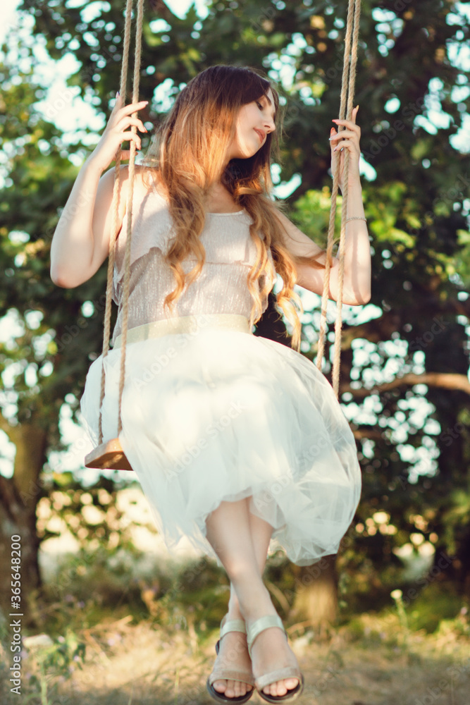 beautiful happy girl with long hair swinging on rope swing on summer nature, young woman enjoy flying in foliage, leisure activity, lifestyle concept