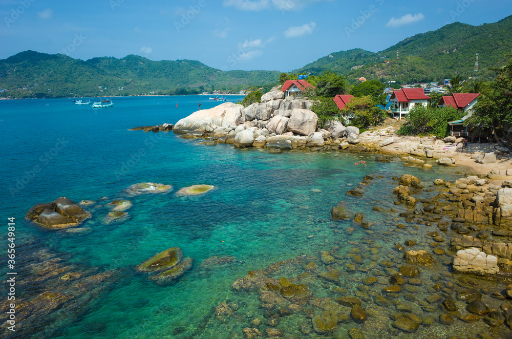 Tropical island coastline, Coast of Koh Tao island with turquoise clear sea water, rocky bottom, houses with red roof dehind granit rocks. Famous destination for travel holidays in Thailand