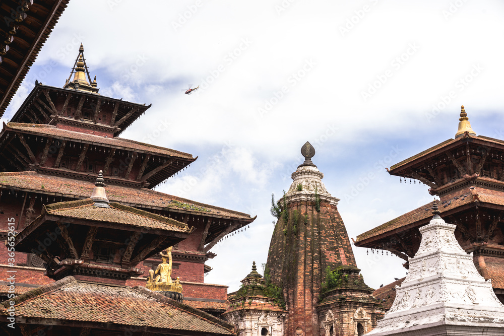 Helicopter flying in the sky under Lalitpur, rooftops of temples and stupas at Patan Durbar Square in Kathmandu, Nepal on a sunny day, religious landmark for Hindu and Buddhist people