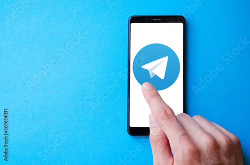 A male hand holds a smartphone, points a finger, types. Communication on a smartphone, correspondence. Place for text. Smartphone in hand on a blue  background.