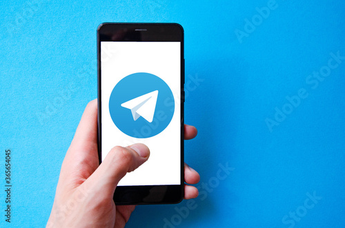 A male hand holds a smartphone, points a finger, types. Communication on a smartphone, correspondence. Place for text. Smartphone in hand on a blue  background.