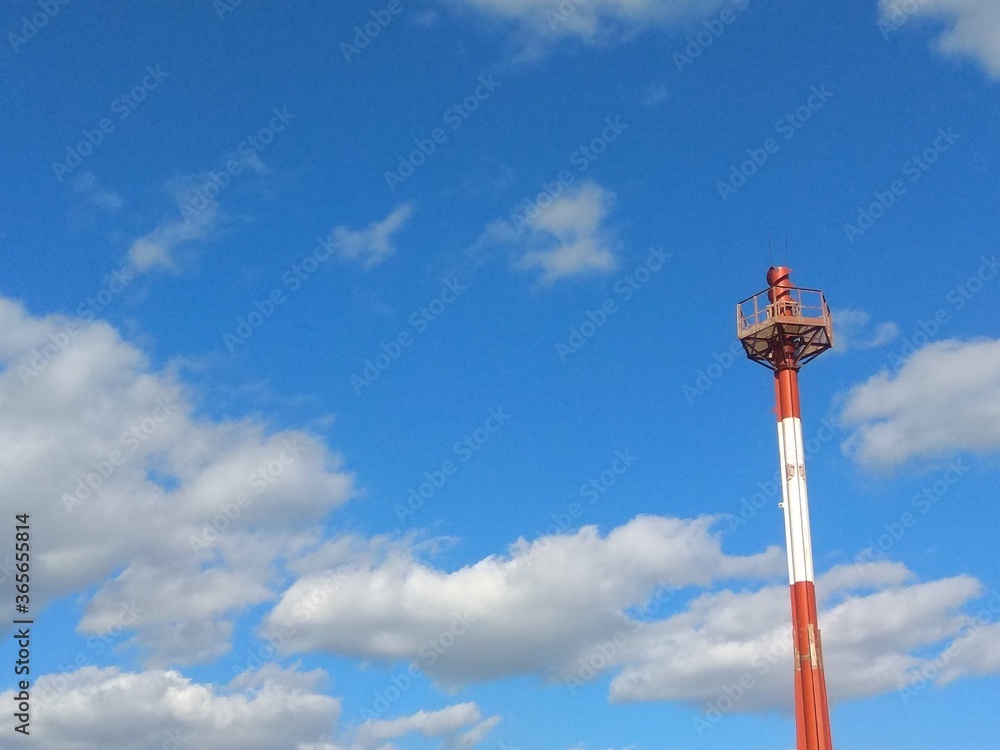 Single red and white radio signal tower with white clouds and blue sky on the background Single red and white radio signal tower with white clouds and blue sky on the background