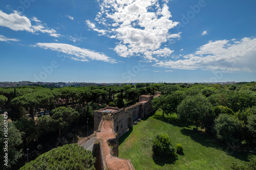 Skyline of the city of Rome and the Aurelian walls of the Roman age. This stretch is at the main entrance of Porta San Sebastiano and is part of the Appia Antica regional park. Sun with clouds. Italy.