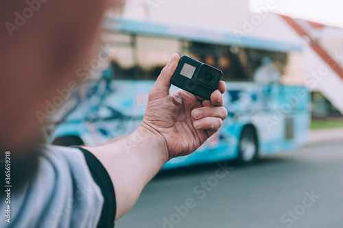 Blogger with an action camera in his hands, against the background of a bus.