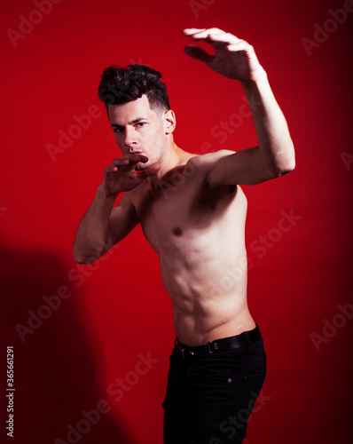 young fashion style man with naked torso dancing emotional posing on red background, lifestyle people concept