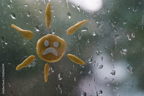 Figure of the sun from plasticine on a wet window. Rainy weather.