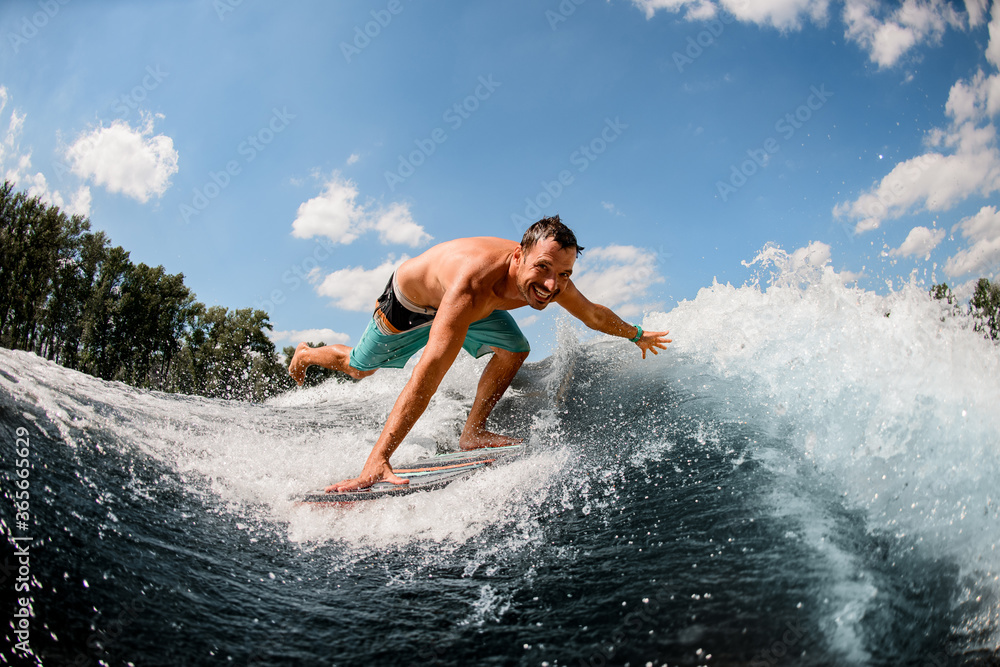 man wakesurfer rides along the wave and touches the spray of water with his hand