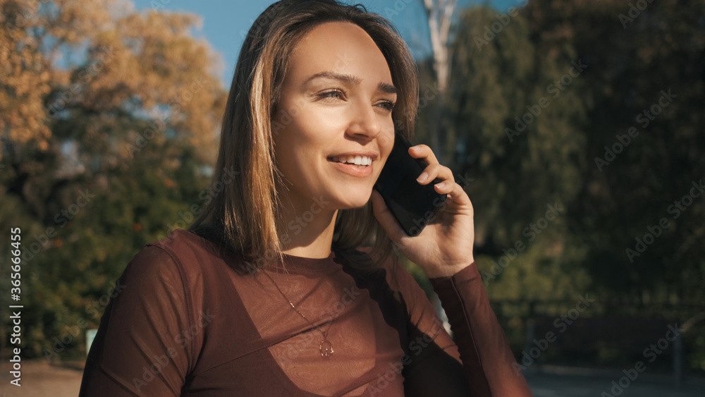 Beautiful smiling girl happily talking on phone with friend during walk along park Beautiful smiling girl happily talking on phone with friend during walk along park