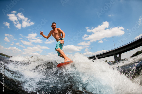 wakesurfer balancing on board on wave against blue sky