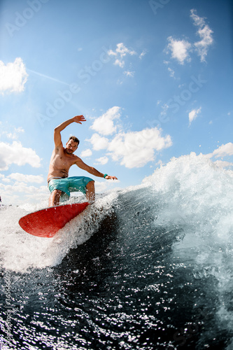 Sporty guy actively ride on the waves on surfboard against blue sky