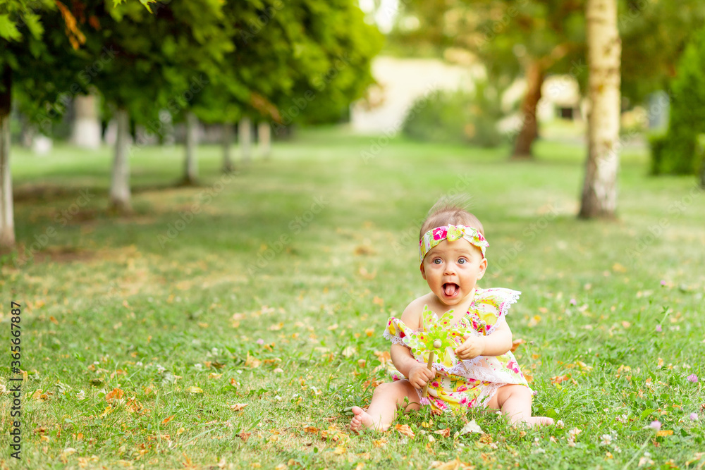 little baby girl 7 months old sitting on a green lawn in a yellow dress and playing with a toy, walking in the fresh air, space for text little baby girl 7 months old sitting on a green lawn in a yellow dress and playing with a toy, walking in the fresh air, space for text