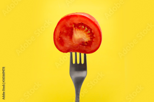 Half a red fresh tomato on a fork on a yellow background