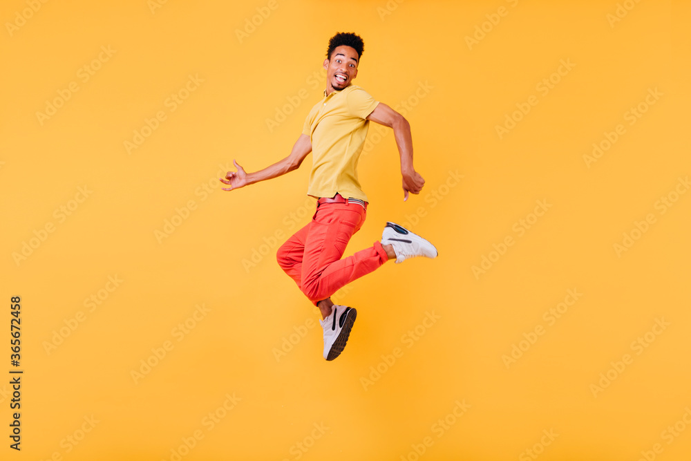 Amazed black male model fooling around on yellow background. Refined short-haired african guy jumping in studio.