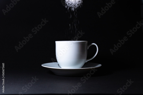 adding sugar to the cup on black background