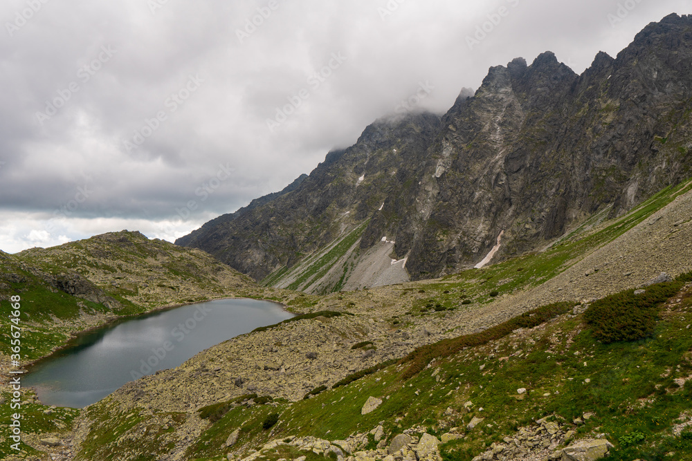 Scenic view of mountains clouds and green with a reflection in a frogs lake. Stony shore. hlincovo pleso. hlincovo lake. High Tatras, Slovakia Concept of nature and tourism Scenic view of mountains clouds and green with a reflection in a frogs lake. Stony shore. hlincovo pleso. hlincovo lake. High Tatras, Slovakia Concept of nature and tourism