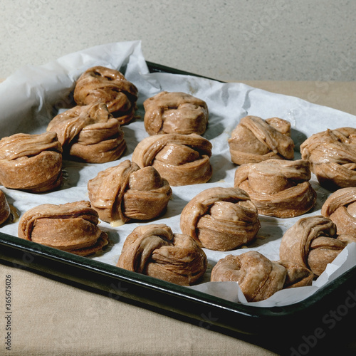 Ready to bake traditional Swedish cinnamon sweet buns Kanelbulle on oven tray cover by baking paper on grey linen table cloth. photo