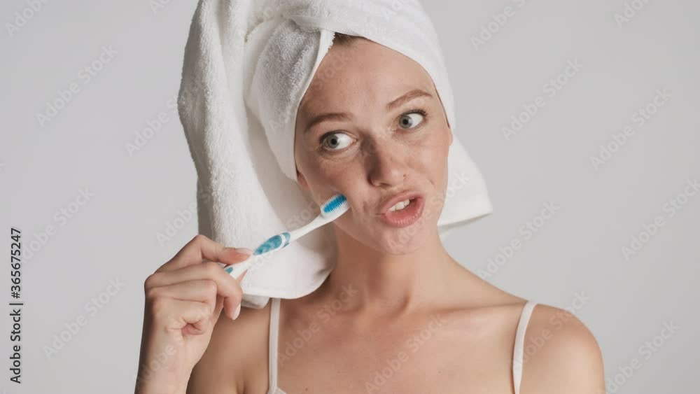 Beautiful smiling girl with towel on head playfully posing on camera with toothbrush over gray background. Fooling around Beautiful smiling girl with towel on head playfully posing on camera with toothbrush over gray background. Fooling around