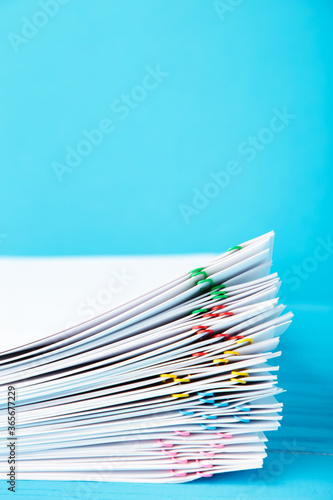 Colorful paper clip with pile of overload white paperwork on blue. Vertical foto