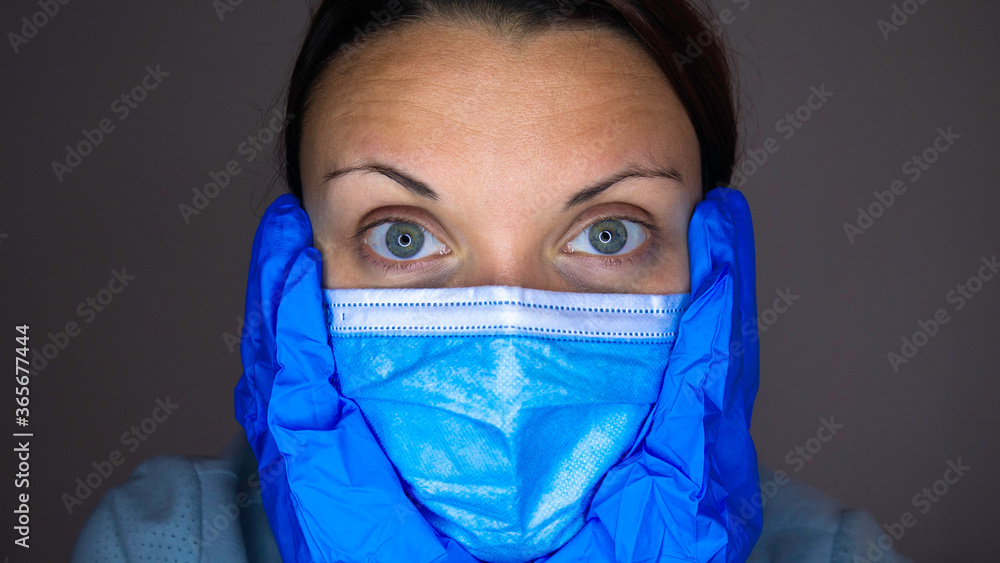Close-up portrait of a woman with blue eyes in a medical mask and blue rubber gloves on her face. Close-up portrait of a woman with blue eyes in a medical mask and blue rubber gloves on her face.