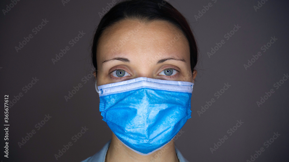Close up portrait of a caucasian woman with sad blue eyes and a blue medical mask on his face. Close up portrait of a caucasian woman with sad blue eyes and a blue medical mask on his face.
