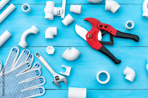 Plastic pipes for the water system, pipe cutting tools, wrench, corners, holders, taps, adapters and work gloves on a light blue background. Top view. photo