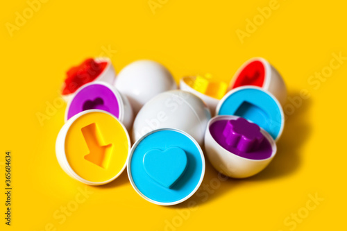 Multicolored plastic eggs on yellow background. An educational sorter toy for toddler to recognize and match colors and shapes. Puzzle montessori game concept. Closeup, copy space for text