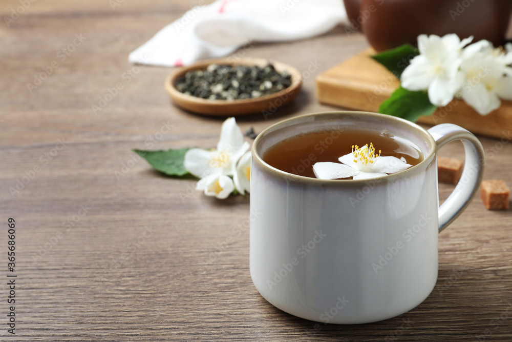 Cup of tea with fresh jasmine flower on wooden table. Space for text Cup of tea with fresh jasmine flower on wooden table. Space for text