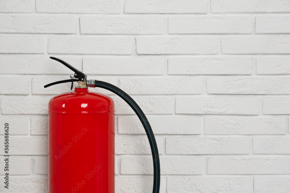 Fototapeta premium Fire extinguisher near white brick wall, closeup. Space for text