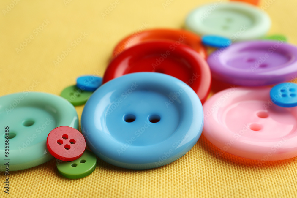 Many bright sewing buttons on yellow fabric, closeup Many bright sewing buttons on yellow fabric, closeup