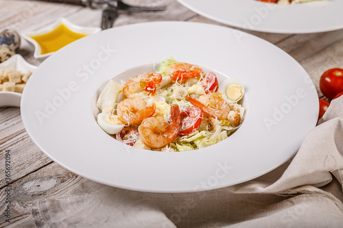 Caesar salad with fried shrimp, quail eggs and parmesan cheese on a white plate. Mediterranean Kitchen. Close-up.