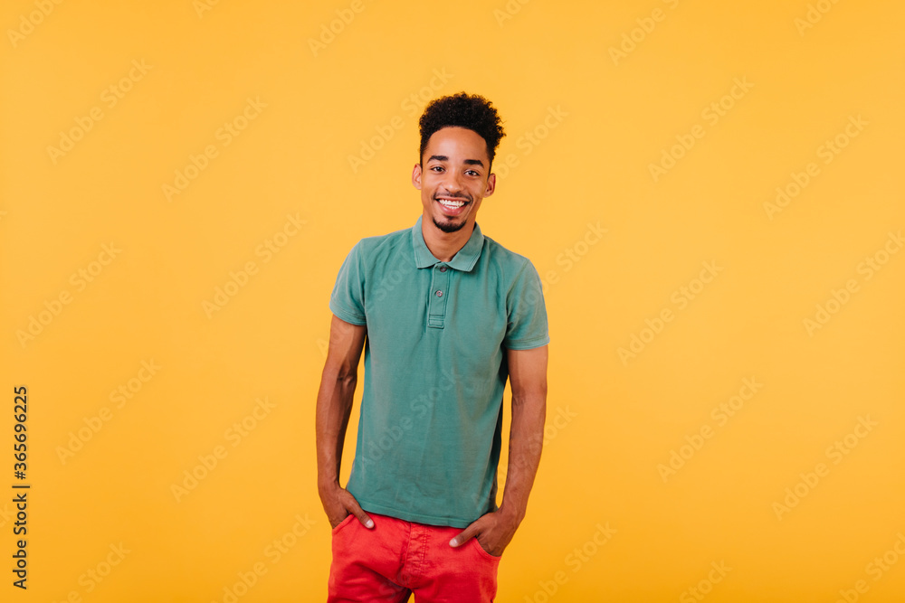 Indoor portrait of smiling black man standing with hands in pockets. Studio shot of blithesome african guy isolated on yellow background. Indoor portrait of smiling black man standing with hands in pockets. Studio shot of blithesome african guy isolated on yellow background.