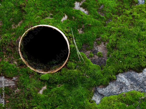 Close up shot of open drainage pipe hole on the wall with moss