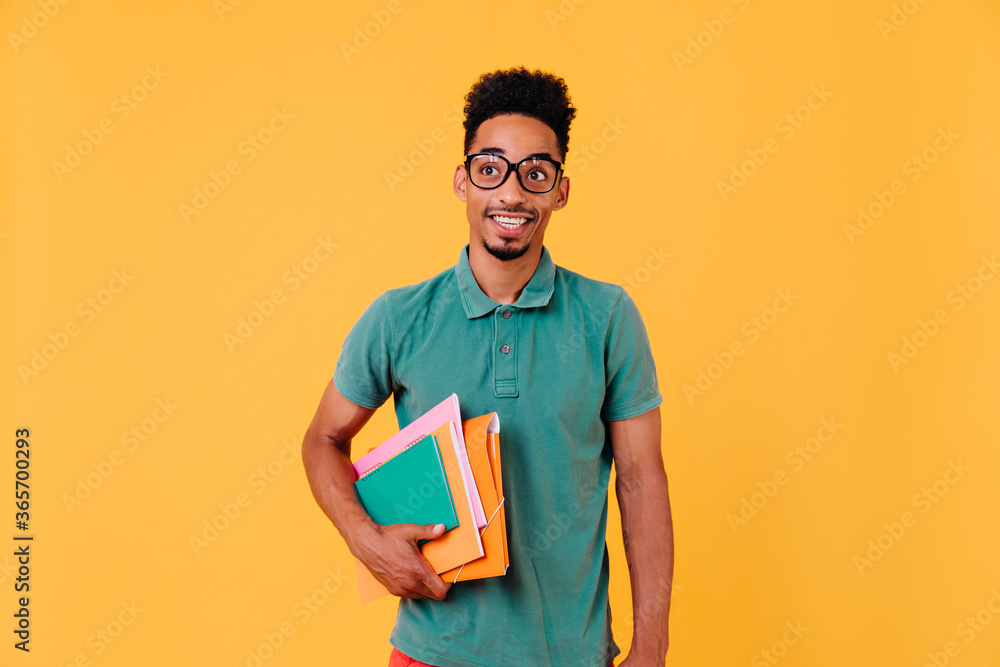 Studio portrait of funny african student in green t-shirt. Photo of blissful black boy in glasses holding books and textbooks after exams. Studio portrait of funny african student in green t-shirt. Photo of blissful black boy in glasses holding books and textbooks after exams.