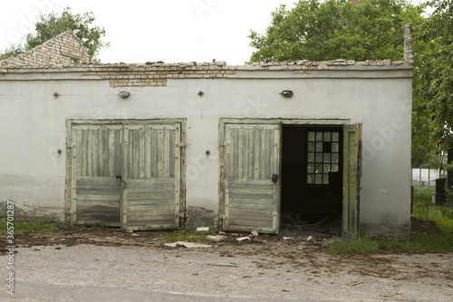 Old white abandoned dilapidated brick garage with wooden green gate doors.  A two-car garage on the territory of a state-owned enterprise. © bela_zamsha