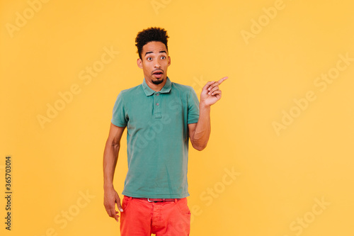 Funny bearded black man posing with amazed face expression. Indoor shot of surprised handsome guy isolated on yellow background.