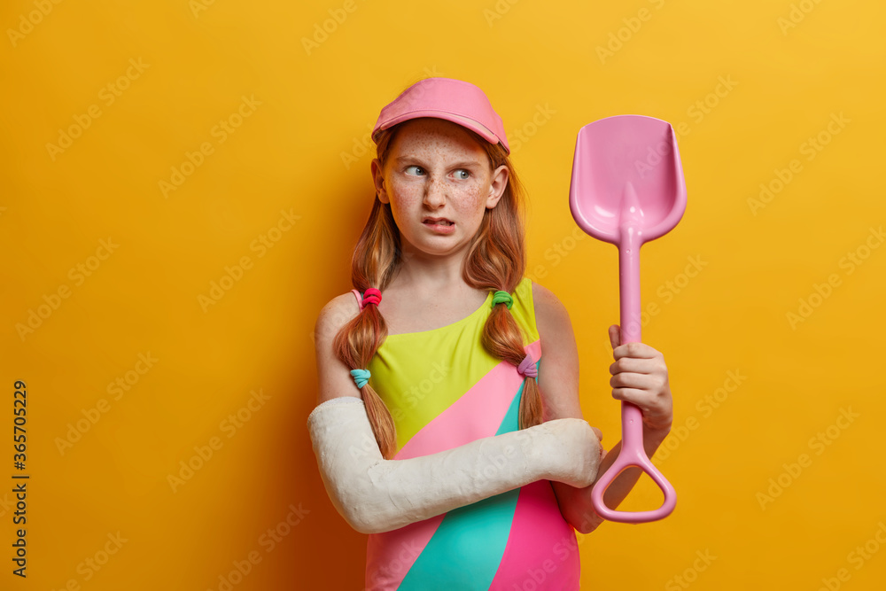 Displeased female child with red hair and freckles looks unhappily at