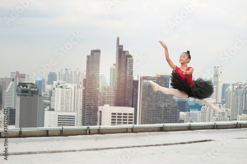Asian ballerina dancer girl jumping in the air, practicing ballet dancing on rooftop with skyscraper city view, adorable child dancing in ballet