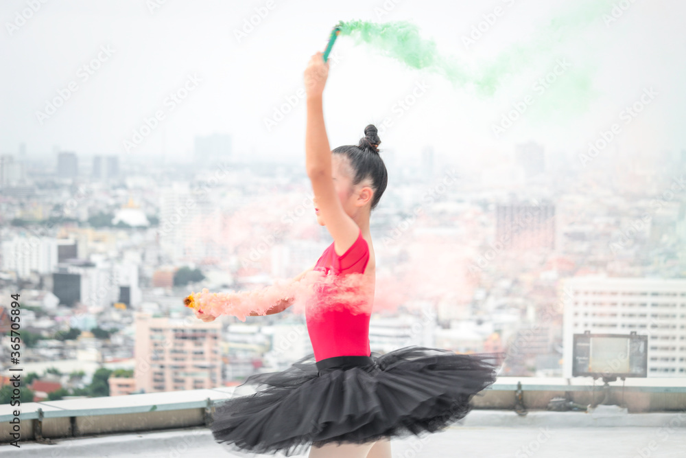 Asian ballerina dancer girl practicing ballet dancing with  colored smoke bomb on rooftop with skyscraper city view, adorable child dancing in ballet