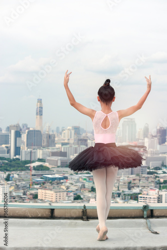 Asian ballerina dancer girl practicing ballet dancing on rooftop with skyscraper city view, adorable child dancing in ballet