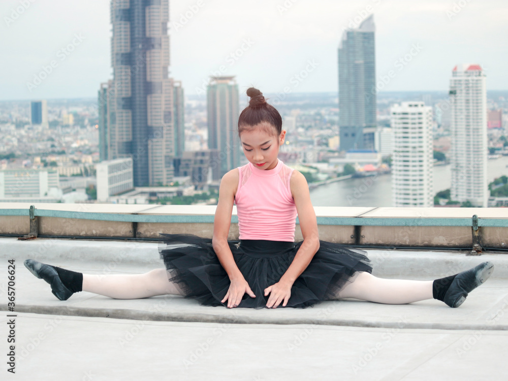 Fototapeta premium Asian ballerina dancer girl practicing ballet dancing on rooftop with skyscraper city view, adorable child dancing in ballet