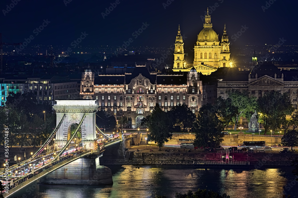 Budapest, Hungary. Fragment of Szechenyi Chain Bridge over Danube, Gresham Palace and St. Stephen's Basilica in night. View from Royal Palace in Buda Castle.